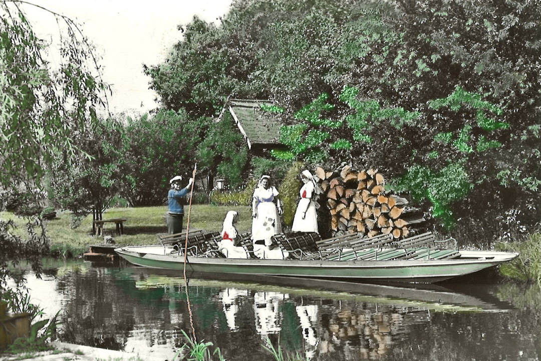 Fährmann und Frauen in Spreewaldtracht vor Erlenholzstapel